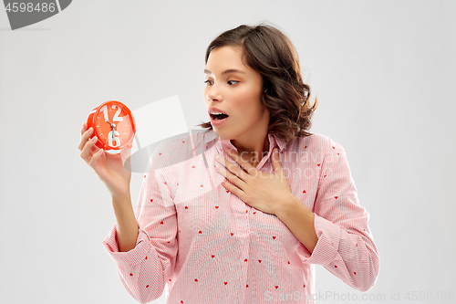 Image of shocked young woman in pajama with alarm clock