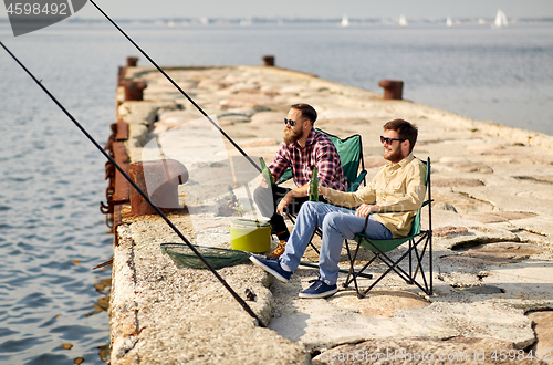 Image of happy friends fishing and drinking beer on pier