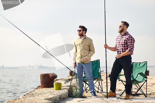 Image of happy friends with fishing rods and beer on pier