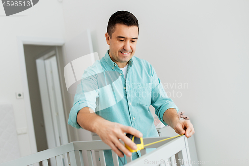 Image of father with tablet pc and ruler measuring baby bed