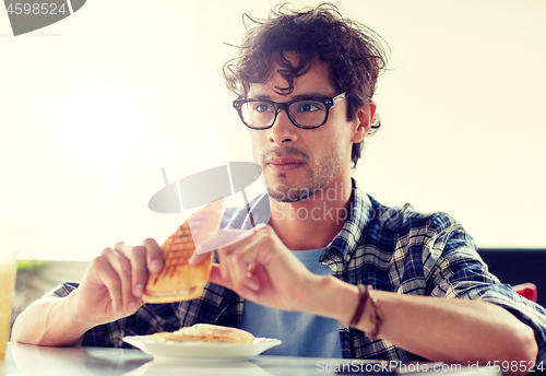 Image of happy man eating sandwich at cafe for lunch