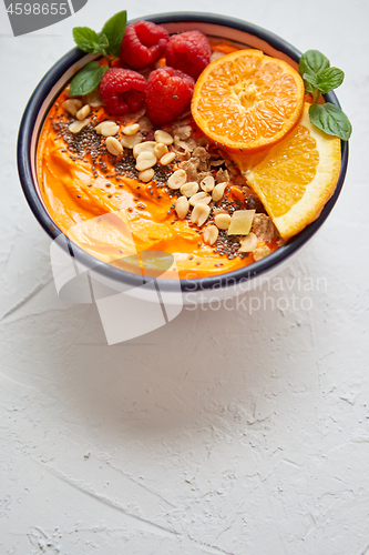 Image of Bowl with fresh healthy smoothie or yogurt. With orange slices, tangerine, raspberry, chia and nuts