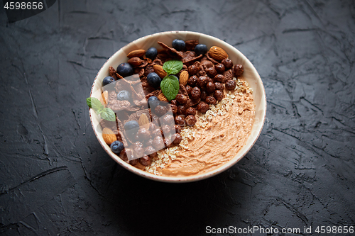 Image of Chocolate and blueberry smoothie or yogurt. With cocoa cornflakes, granola, mint leaves and almonds