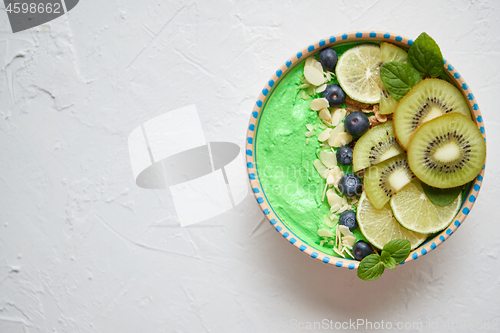 Image of Green smoothie or yogurt bowl. With fresh kiwi, blueberries, lim