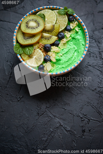 Image of Green smoothie or yogurt bowl. With fresh kiwi, blueberries, lime and almond flakes