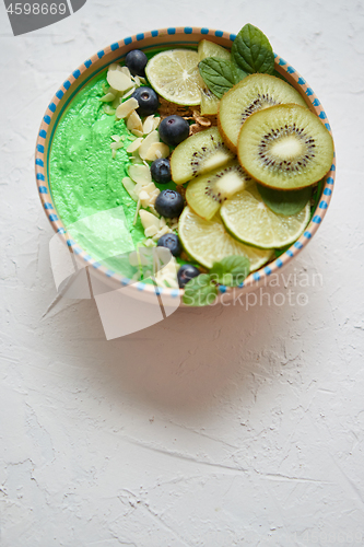 Image of Green smoothie or yogurt bowl. With fresh kiwi, blueberries, lim