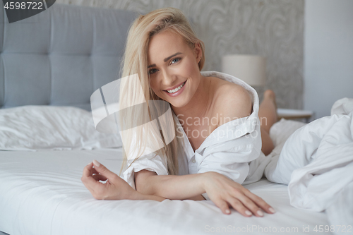 Image of Beautiful middle aged woman lying on the bed, wearing white shirt and smiling