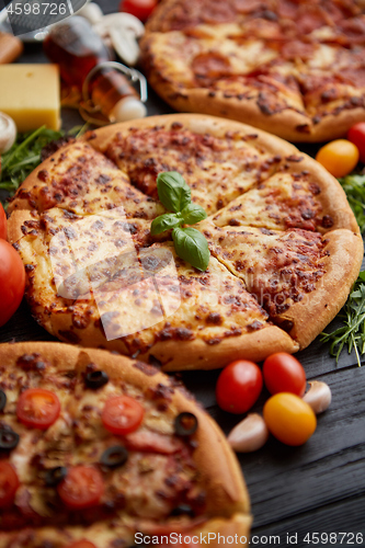 Image of Freshly served, three various pizzas placed among tasty ingredients. Top view