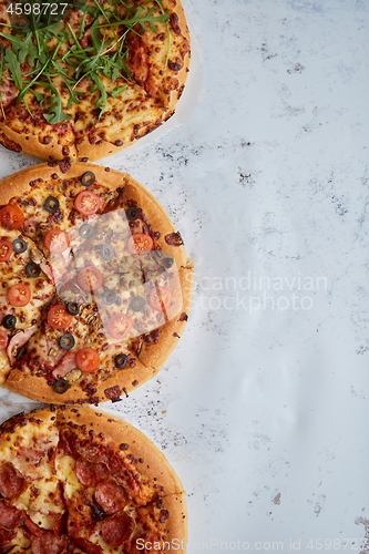 Image of Three different kind of pizzas placed in a row on white rusty ta