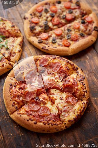 Image of Composition of three various kinds pizzas on wooden table