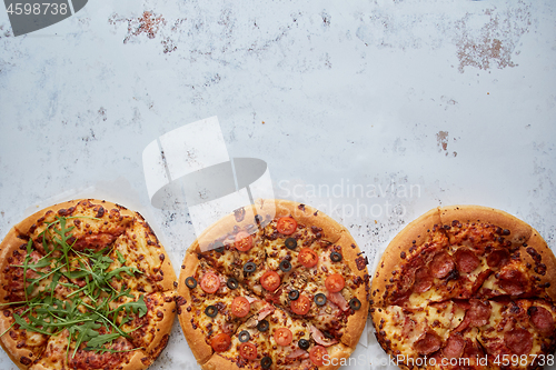 Image of Three different kind of pizzas placed in a row on white rusty ta