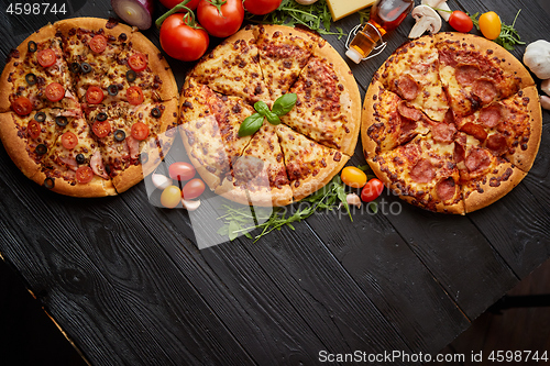 Image of Freshly served, three various pizzas placed among tasty ingredients. Top view