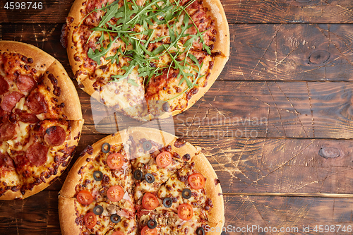 Image of Composition of three various kinds pizzas on wooden table