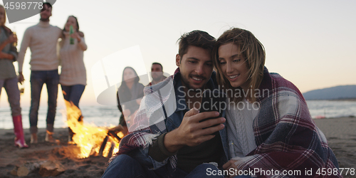 Image of Couple enjoying bonfire with friends on beach