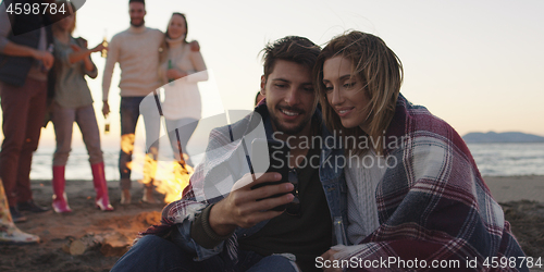 Image of Couple enjoying bonfire with friends on beach