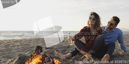 Image of Loving Young Couple Sitting On The Beach beside Campfire drinkin