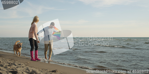 Image of couple with dog having fun on beach on autmun day