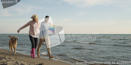 Image of couple with dog having fun on beach on autmun day