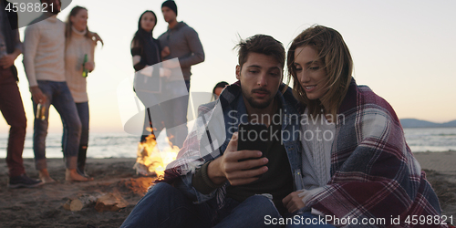 Image of Couple enjoying bonfire with friends on beach