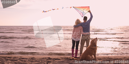 Image of couple with dog having fun on beach on autmun day