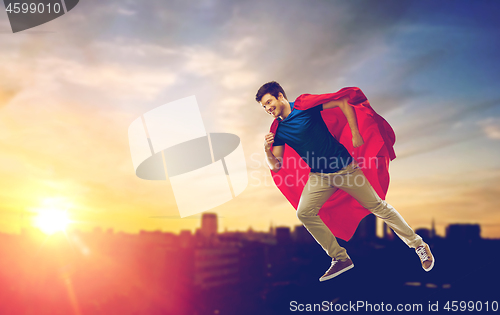 Image of man in superhero cape flying over sunset in city