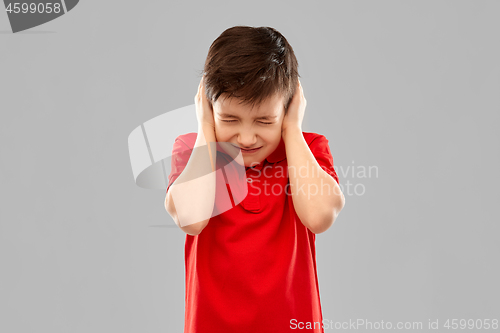 Image of stressed boy in red t-shirt closing ears by hands