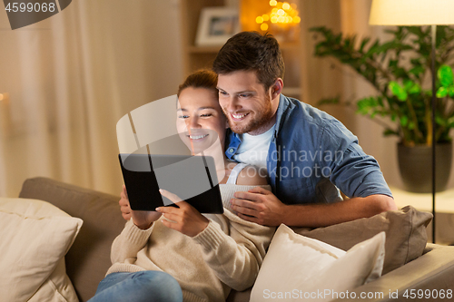 Image of happy couple using tablet pc at home in evening