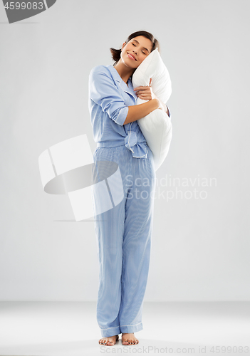 Image of happy young woman in blue pajama hugging pillow