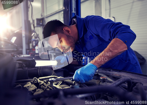 Image of mechanic man with lamp repairing car at workshop