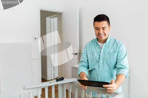 Image of father with tablet pc assembling baby bed at home