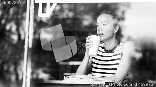 Image of Young caucasian woman sitting alone in coffee shop thoughtfully leaning on her hand, looking trough the window