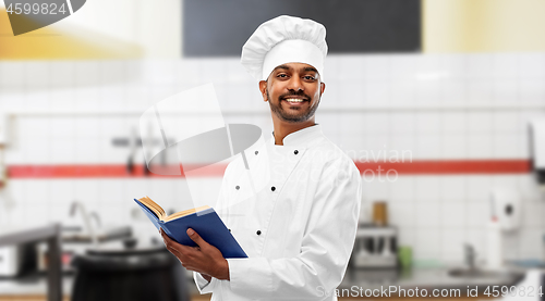 Image of happy indian chef with cookbook at kitchen