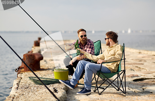 Image of happy friends fishing and drinking beer on pier