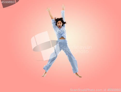 Image of happy woman in blue pajama jumping high over pink