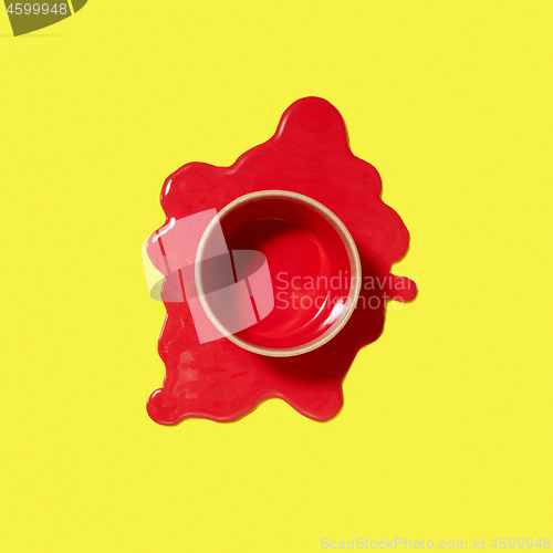 Image of Spilled red puddle of paint with can on an yellow background.