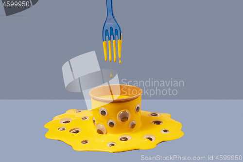 Image of Plastic fork and drops of yellow paint above can in puddle with googly eyes.