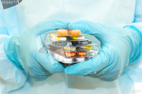 Image of Nurse in a sterile gown and gloves holds packs of pills in blisters