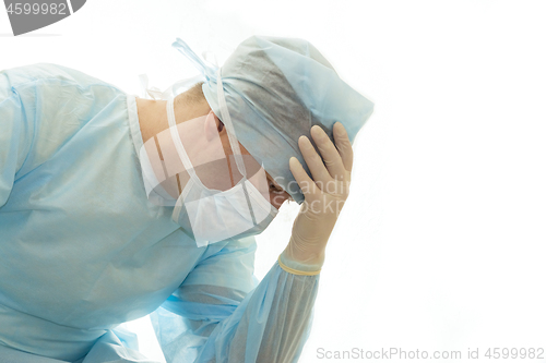 Image of Upset surgeon in sterile gown and surgical mask props his head with hand