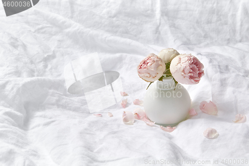 Image of Vase with fresh roses on crumpled sheets.