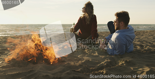 Image of Loving Young Couple Sitting On The Beach beside Campfire drinkin