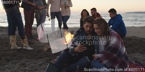 Image of Couple enjoying bonfire with friends on beach