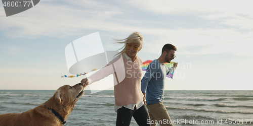 Image of couple with dog having fun on beach on autmun day