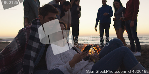 Image of Couple enjoying bonfire with friends on beach