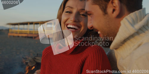 Image of Loving Young Couple Sitting On The Beach beside Campfire drinkin