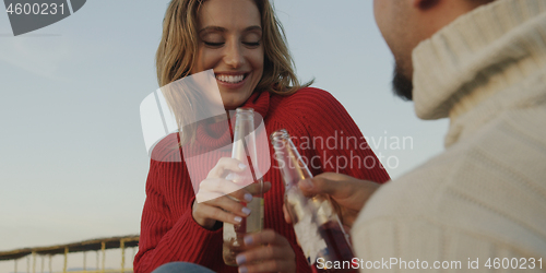 Image of Loving Young Couple Sitting On The Beach beside Campfire drinkin