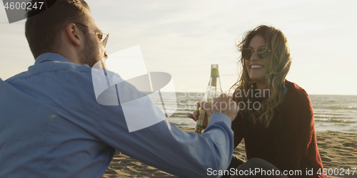 Image of Loving Young Couple Sitting On The Beach beside Campfire drinkin