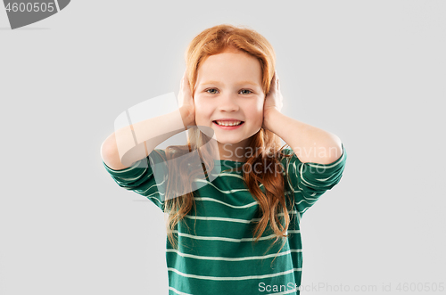 Image of smiling red haired girl closing ears by hands