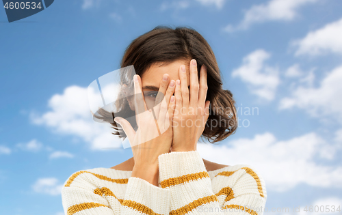 Image of young woman looking by one eye through her fingers