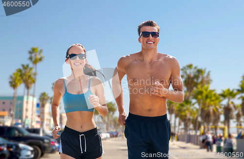 Image of couple in sports clothes running along on beach