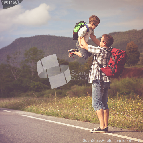 Image of Father and son walking on the road at the day time.